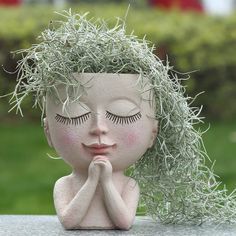 a ceramic doll with eyes closed and grass growing on her head