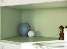 two vases sitting on top of a green shelf next to a white cabinet door