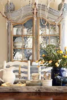 a dining room table with plates and vases on it, next to a china cabinet