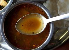 a spoon full of soup sitting on top of a metal bowl filled with food next to bread