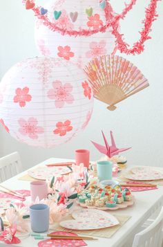 the table is set with plates, cups and paper lanterns