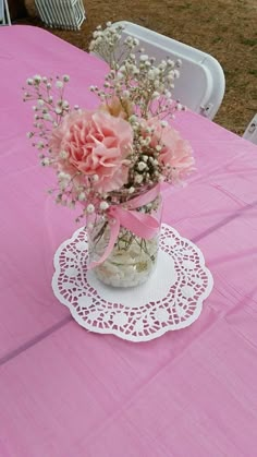 pink flowers in a vase on a doily at a table with chairs and tablescloths