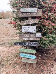 a wooden sign sitting in the middle of a field next to a tree and bushes