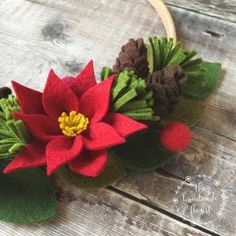 felt poinsettia with green leaves and red flowers on wooden table next to hoop