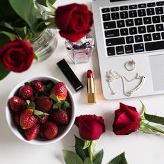 a white table topped with a bowl of strawberries next to a laptop and roses