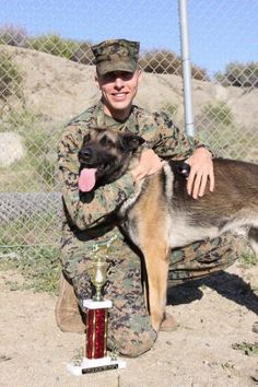 a man kneeling down next to a dog holding a trophy