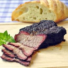 a piece of meat sitting on top of a wooden cutting board next to a loaf of bread