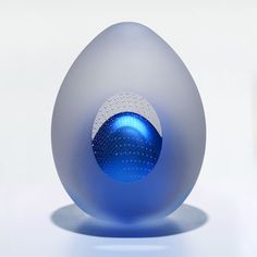 an egg shaped object sitting on top of a white table next to a blue vase