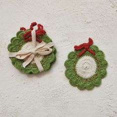 two crocheted christmas ornaments hanging on a wall next to each other, one green and the other red