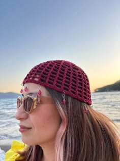 a woman wearing sunglasses and a crocheted hat looks out over the water at sunset