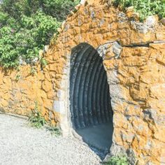 an old stone tunnel in the side of a wall with plants growing out of it