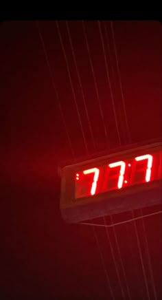 an electronic clock displaying the time on a red light in the dark, with wires above it