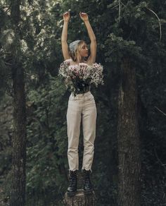 a woman standing on top of a tree stump with flowers in her hands and arms up