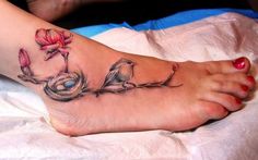 a woman's foot with two birds on it and flowers in the middle, sitting on a bed