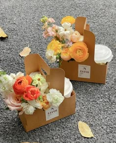 two boxes with flowers in them sitting on the ground next to plates and napkins