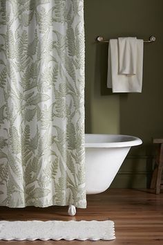 a bath tub sitting next to a white towel on top of a wooden floor in front of a green wall