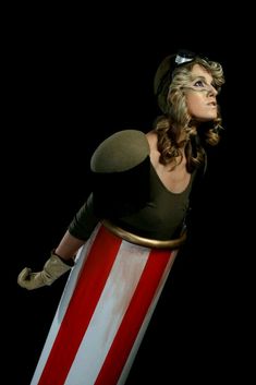 a woman is dressed in an american flag costume and holding a giant red white and blue object