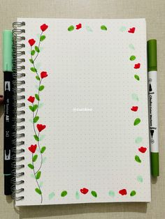 an open notebook with red flowers and green leaves on the cover next to a marker