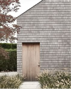 a wooden door in front of a gray brick building with tall grass and trees around it