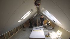 two men are working in an attic with white walls and wood beams on the floor