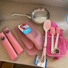 pink utensils are sitting on the counter next to a pan and measuring spoons