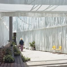 a woman walking down a sidewalk next to a white wall covered in plastic coverings