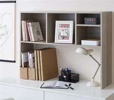 a white desk topped with books and a lamp next to a wall mounted art piece