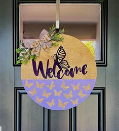 a welcome sign hanging on a door with butterflies around it and the word welcome written in purple