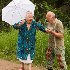 an older man and woman standing next to each other on a skateboard with an umbrella