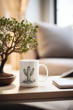 a coffee mug with a cactus on it sitting next to a small potted plant