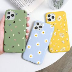 three phone cases with daisies and hearts are sitting on a table next to an open book