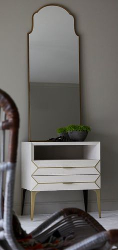 a white dresser sitting next to a mirror on top of a wooden table with a plant in it