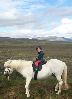 a young boy riding on the back of a white horse in a field with mountains in the background