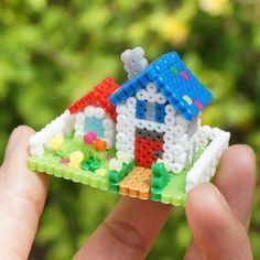 a hand holding a small toy house made out of beads