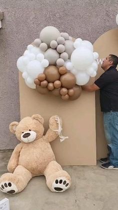 a man standing next to a giant teddy bear with balloons on it's head