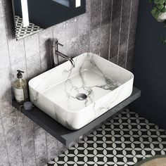 a white sink sitting on top of a black and white tiled bathroom counter next to a mirror