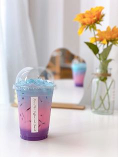 a plastic cup filled with liquid sitting on top of a table next to a vase full of flowers