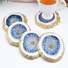 four blue and white plates with gold rims next to a tea cup on a table