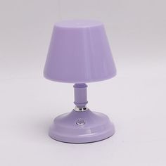 a purple table lamp on a white surface with a light bulb turned on and the shade off