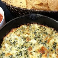 a pizza in a skillet next to some chips and salsa on a table with a bowl of guacamole