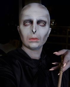 a man with white makeup and black make up holding a wooden stick in his hand