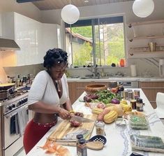 a woman standing at a kitchen counter cutting food on top of a wooden cutting board