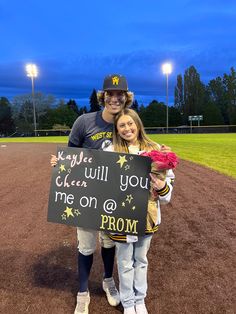 a man and woman standing on a baseball field holding a sign