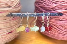 three different colored beads are hanging from a knitting needle next to some balls of yarn