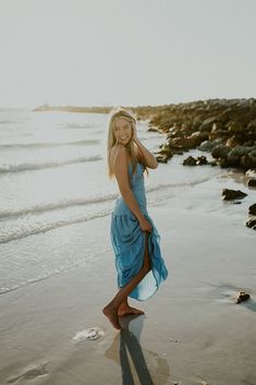 a woman in a blue dress standing on the beach