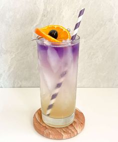 a purple drink with an orange slice on the rim and a striped straw garnish