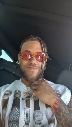 a man with dreadlocks and red sunglasses sitting in a car