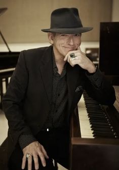 a man in a black suit and hat sitting at a piano with his hands on his chin