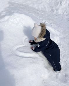 a small child is laying in the snow with his head down and wearing a hat