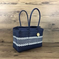 a blue and white woven bag sitting on top of a wooden table next to a wall